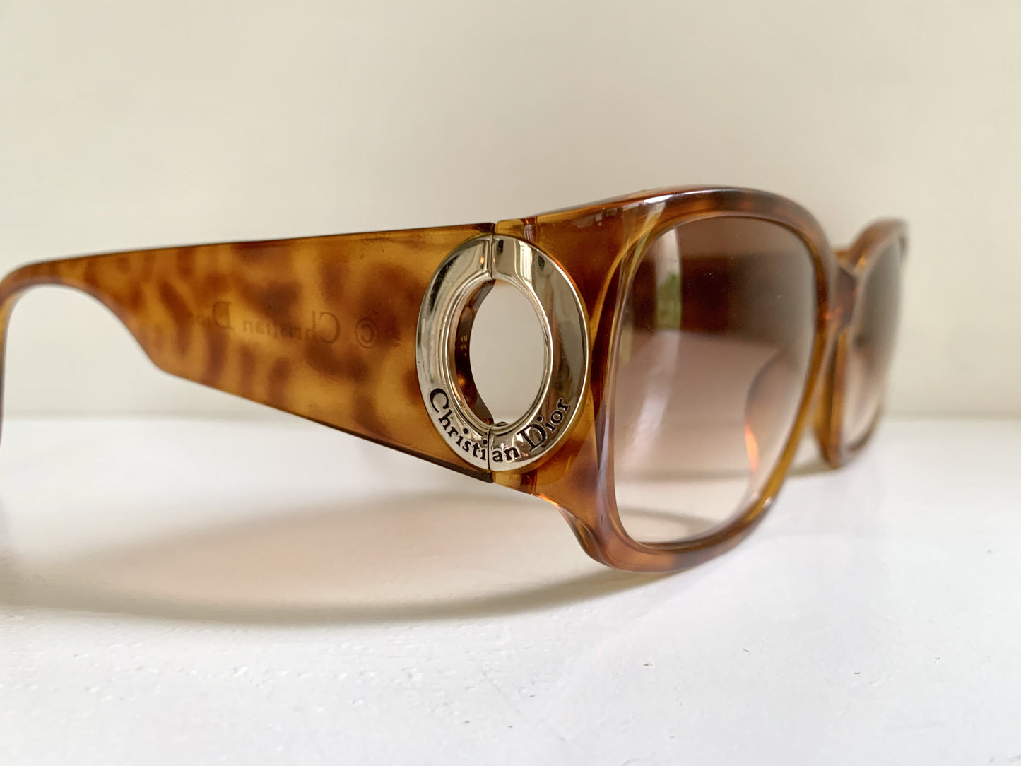 Sunglasses with a tortoiseshell frame and gold logo on a white surface.