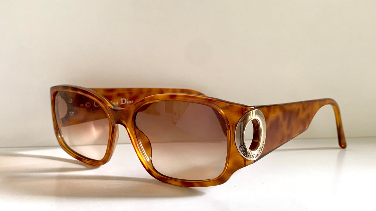 Brown tortoiseshell sunglasses with a Dior logo on a white background