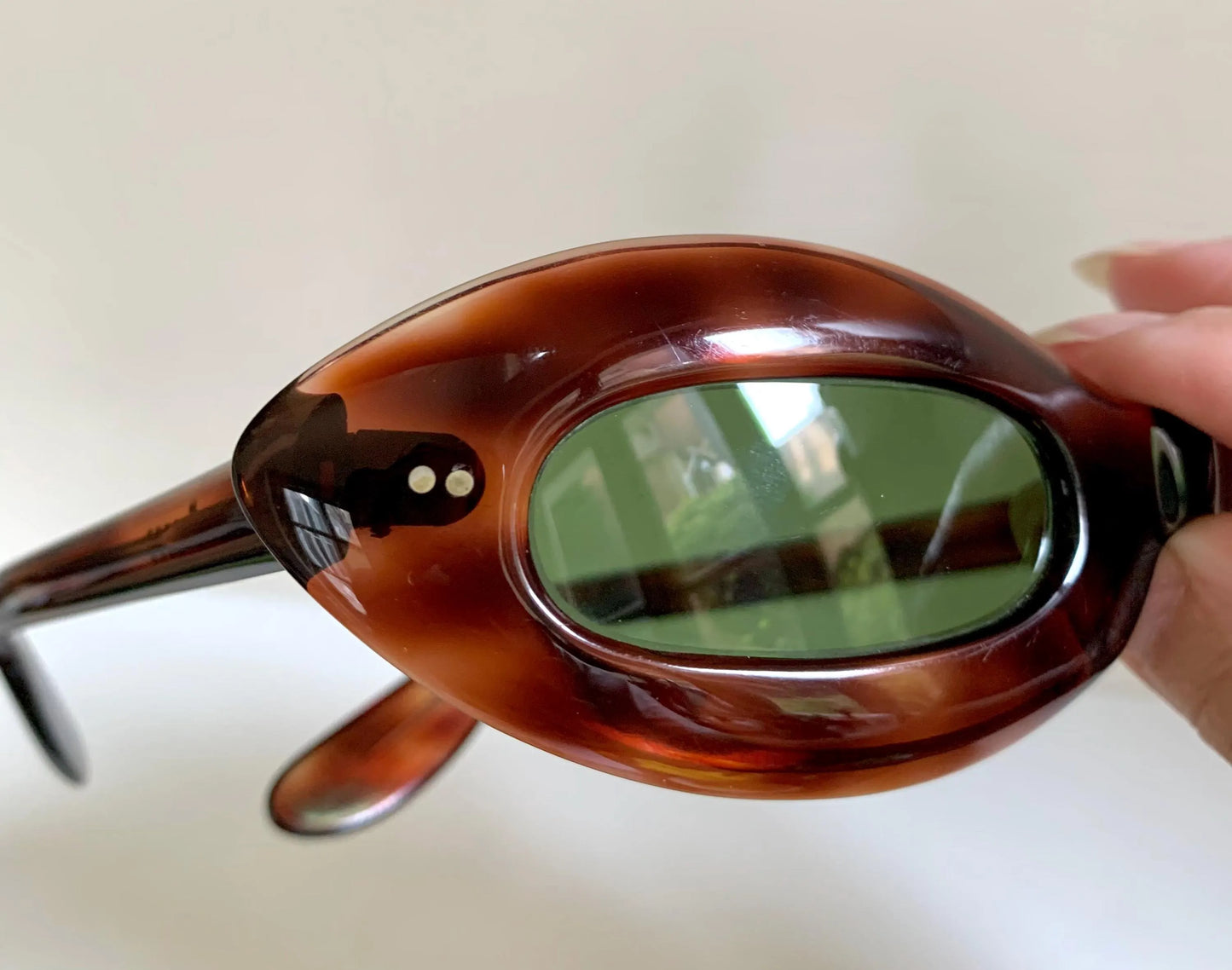Tortoiseshell sunglasses with green lenses held by a hand against a neutral background
