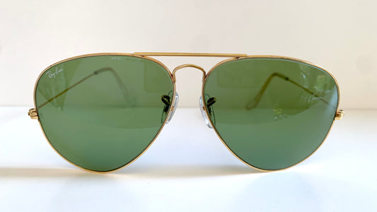Aviator sunglasses with gold frame and green lenses on a white background