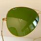 Gold-framed sunglasses with green lenses on a light background