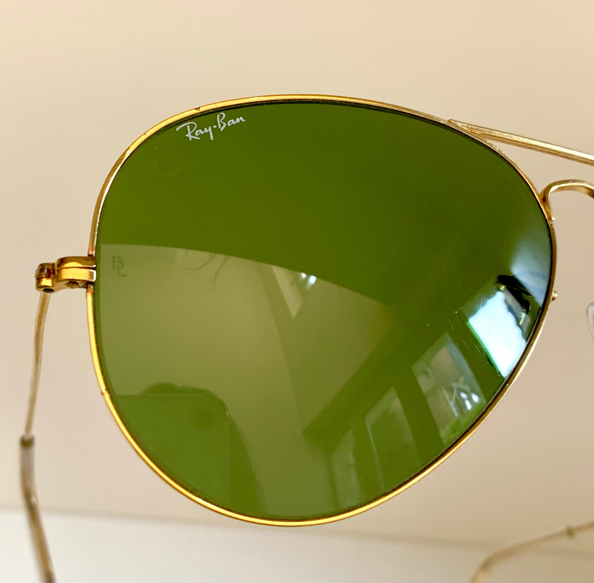 Gold-framed sunglasses with green lenses on a light background