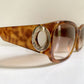 Sunglasses with a tortoiseshell frame and gold logo on a white surface.