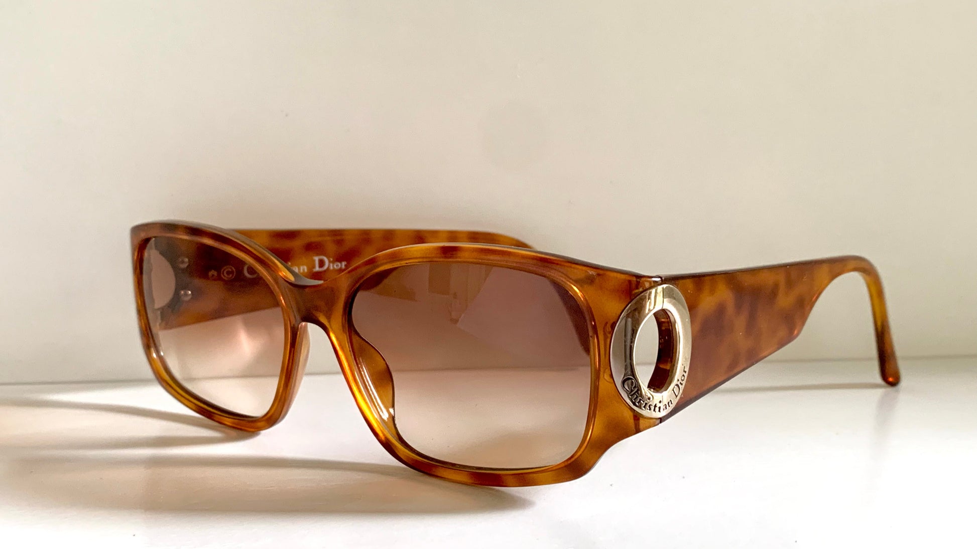 Brown tortoiseshell sunglasses with a Dior logo on a white background