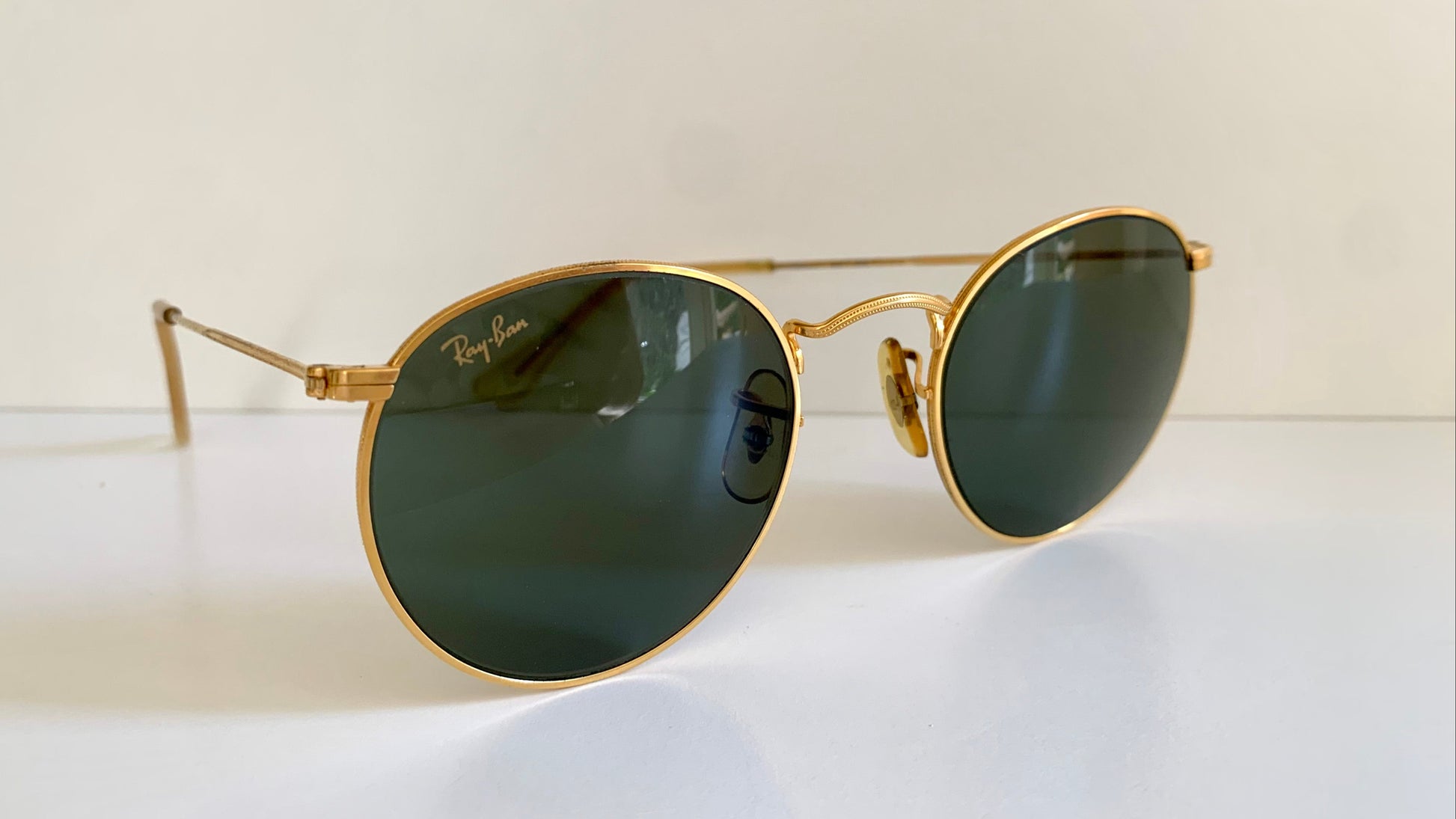 Ray Ban round sunglasses with gold frame and green lenses on a white background