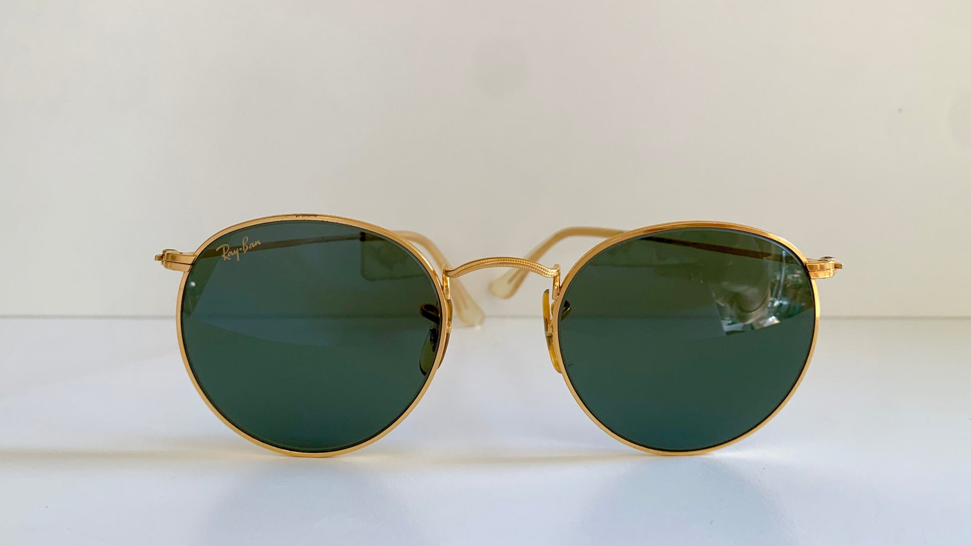 Ray Ban round sunglasses with gold frame and green lenses on a white background