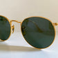 Round sunglasses with gold frame and dark lenses on a light background