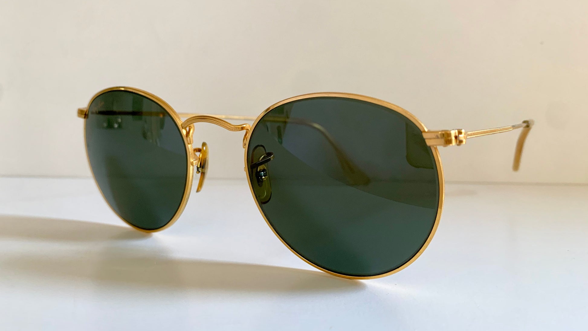 Round sunglasses with gold frame and dark lenses on a light background