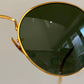 Gold-framed sunglasses with dark lenses on a light gray background