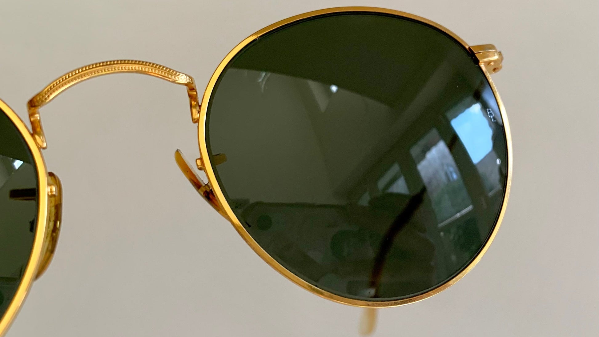 Gold-framed sunglasses with dark lenses on a light gray background