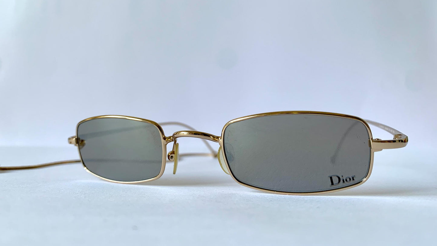 Gold-framed sunglasses with 'Dior' logo on a light gray background