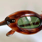 Tortoiseshell sunglasses with green lenses held by a hand against a neutral background